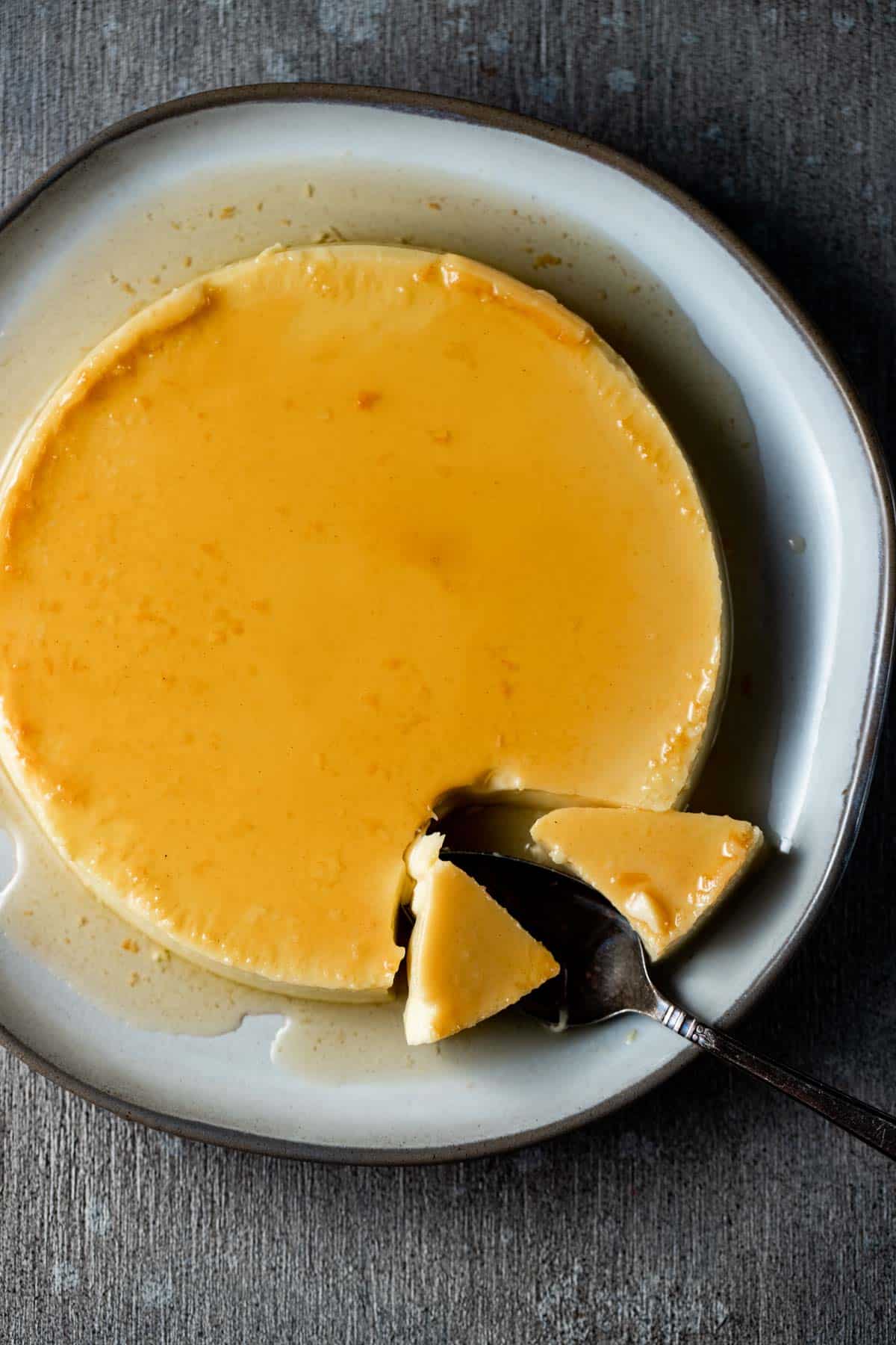 Overhead view of flan on a plate with some pieces removed with a serving utensil.