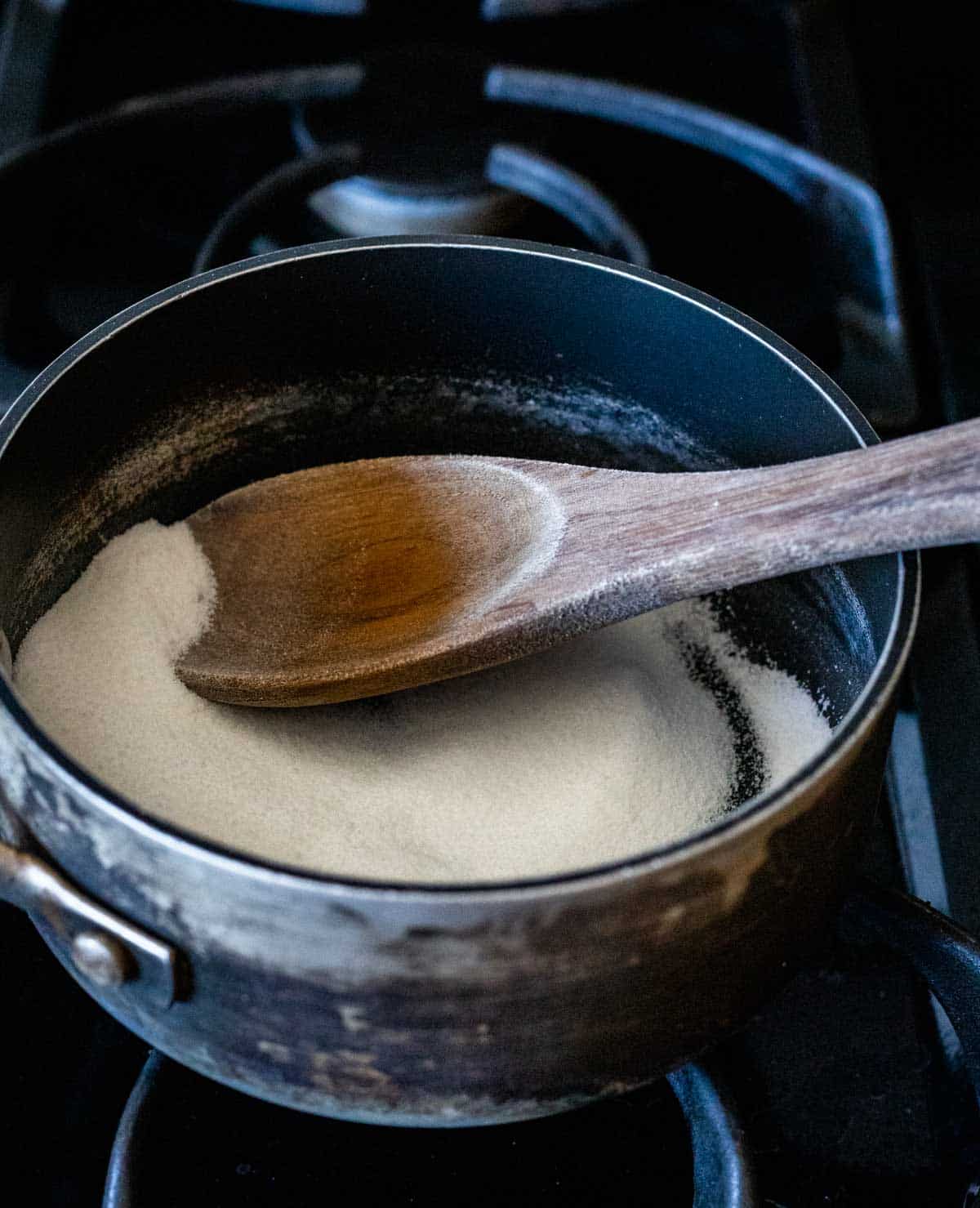 Granulated sugar being stirred around in a sauce pan with a wooden spoon.