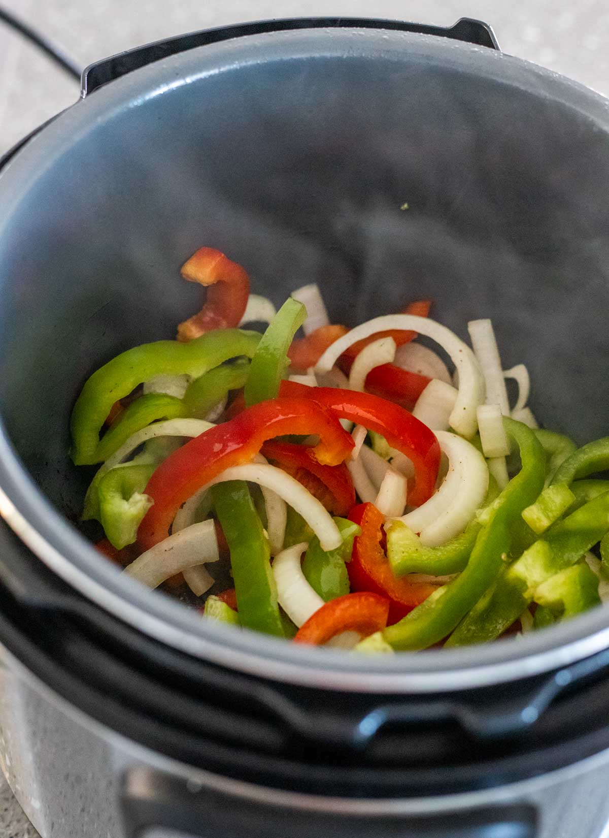 Sliced peppers and onions being sautéed in the Instant Pot insert.