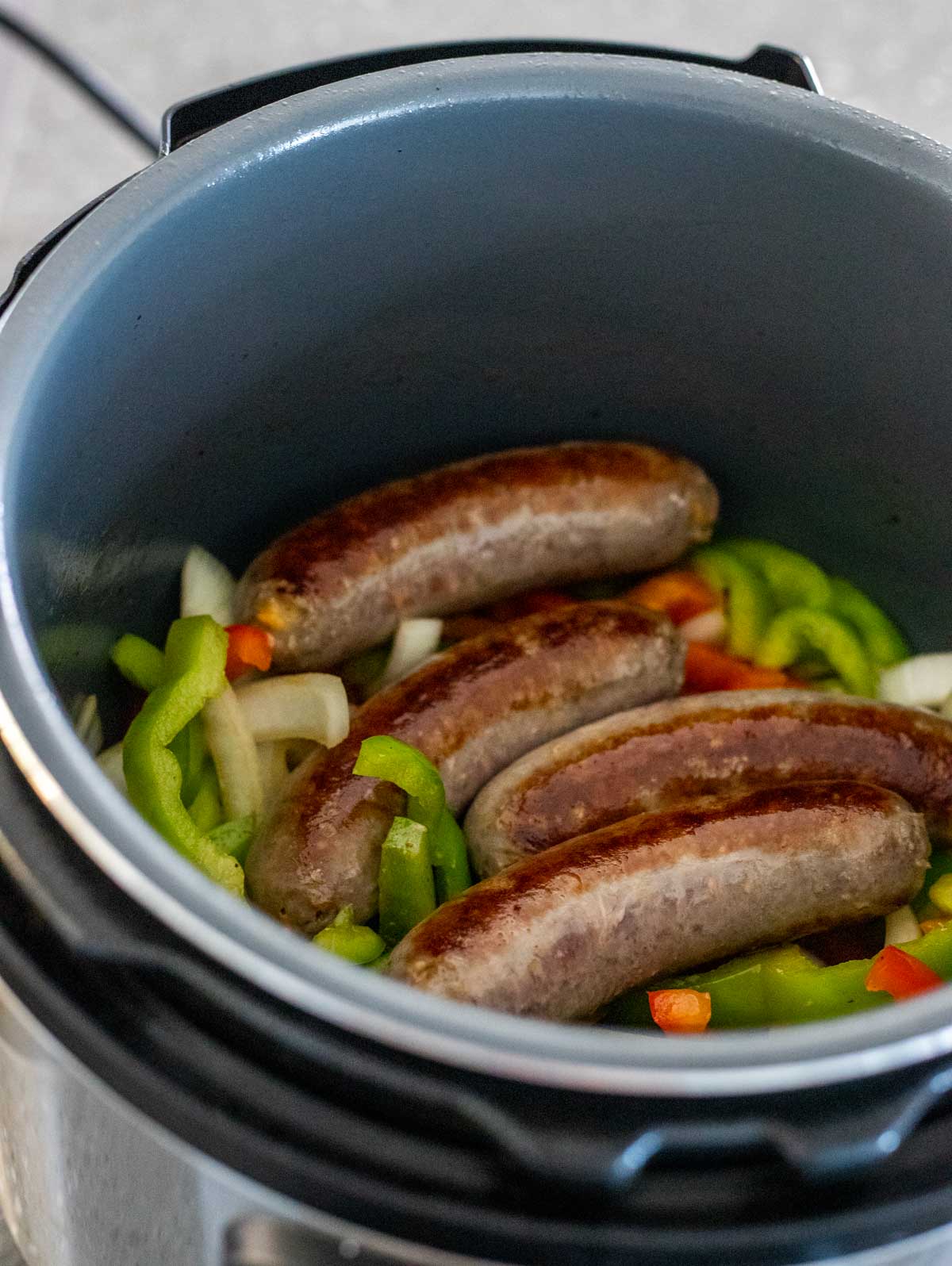 Browned sausages on top of the sautéed onions and peppers in the Instant Pot insert.