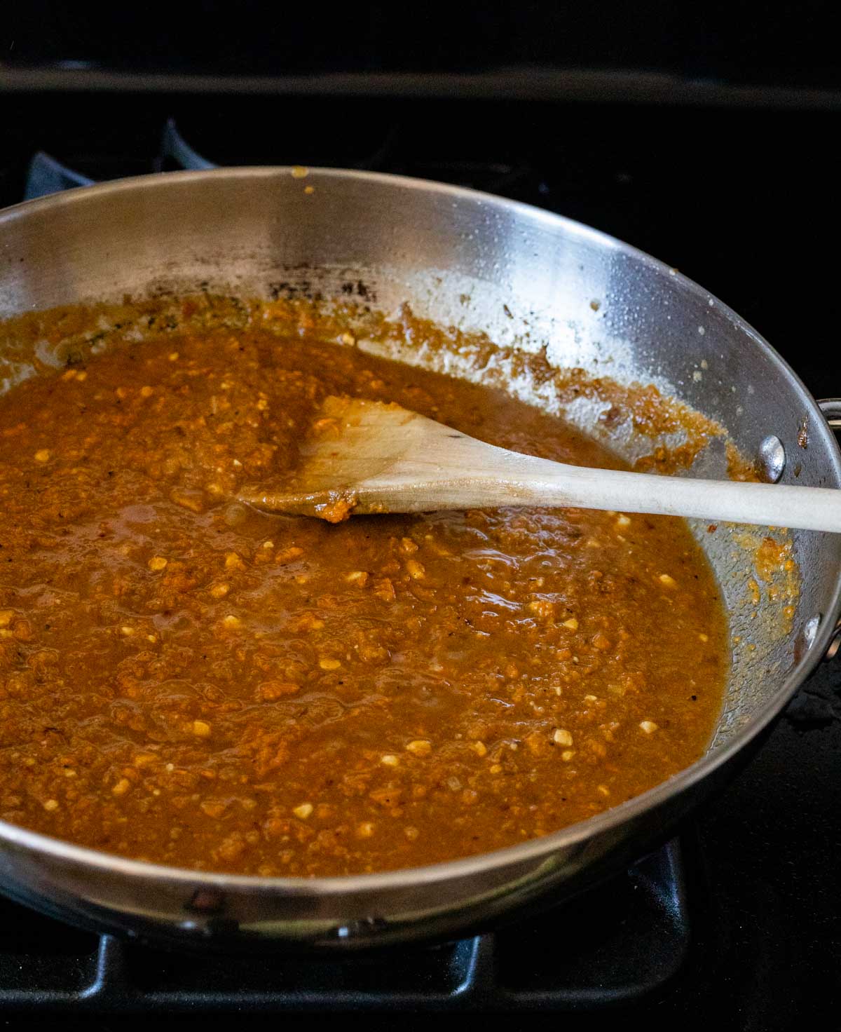 Sweet potato gravy in a skillet and being stirred with a wooden spoon.