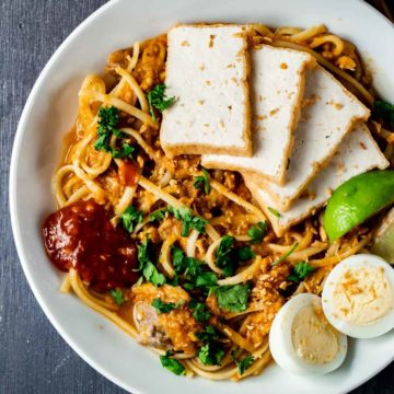 Overhead view of mee rebus in a bowl with tofu, hard boiled eggs and sambal.