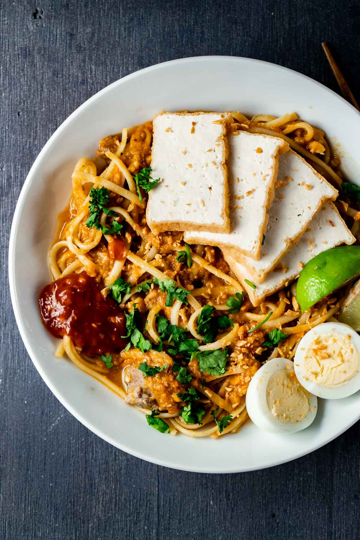 Overhead view of mee rebus in a bowl with tofu, hard boiled eggs and sambal.
