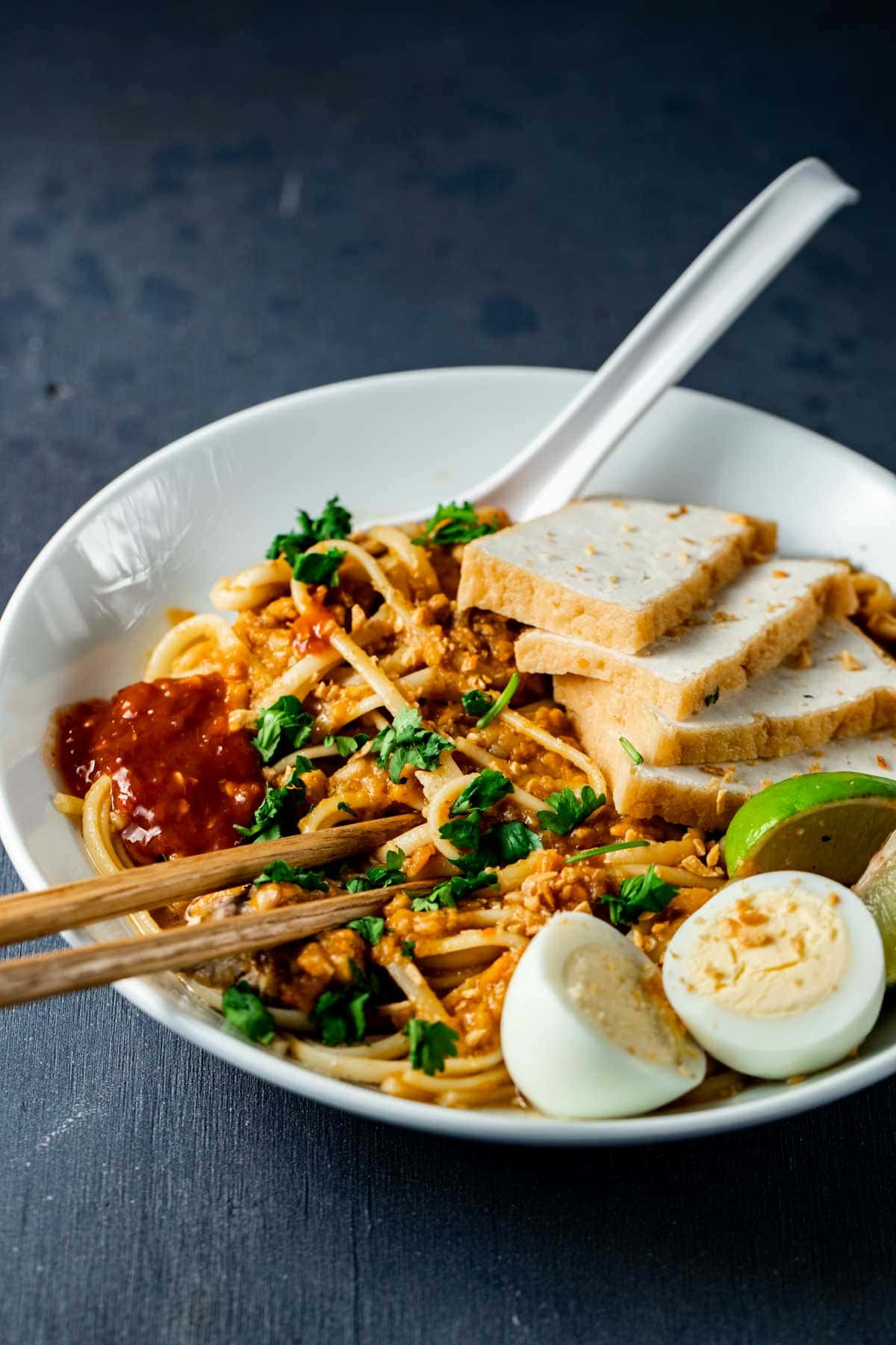 Side view of mee rebus in a bowl topped with tofu and hard boiled eggs.