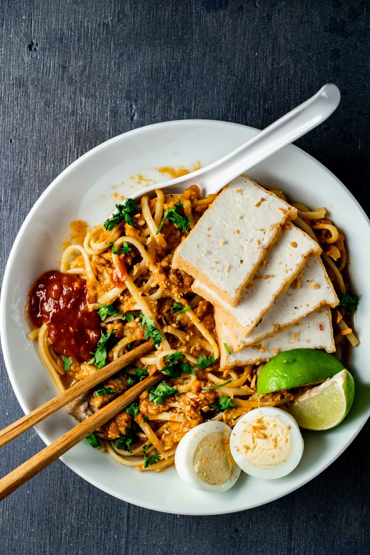 Overhead view of mee rebus with tofu, lime wedges and hard boiled eggs.