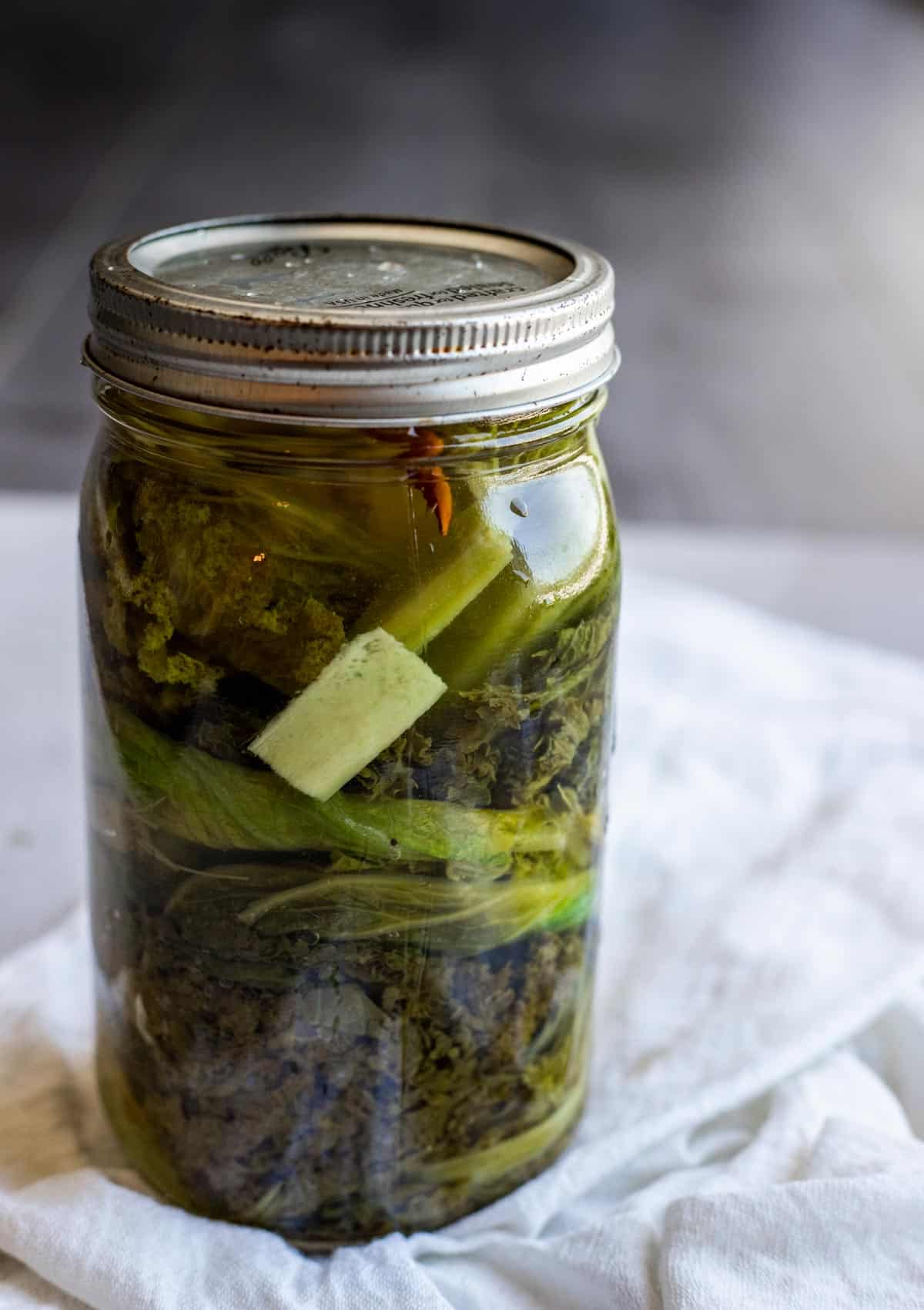 Pickled mustard greens in a glass jar with a lid.