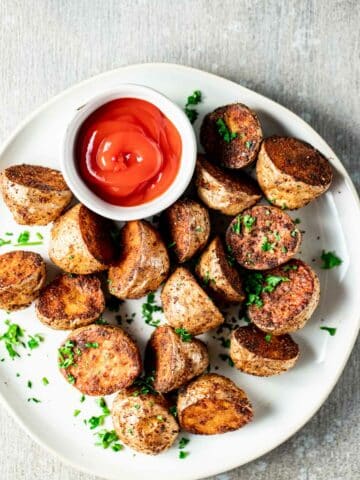 Overhead view of air fried baby potatoes on a white plate with ketchup.