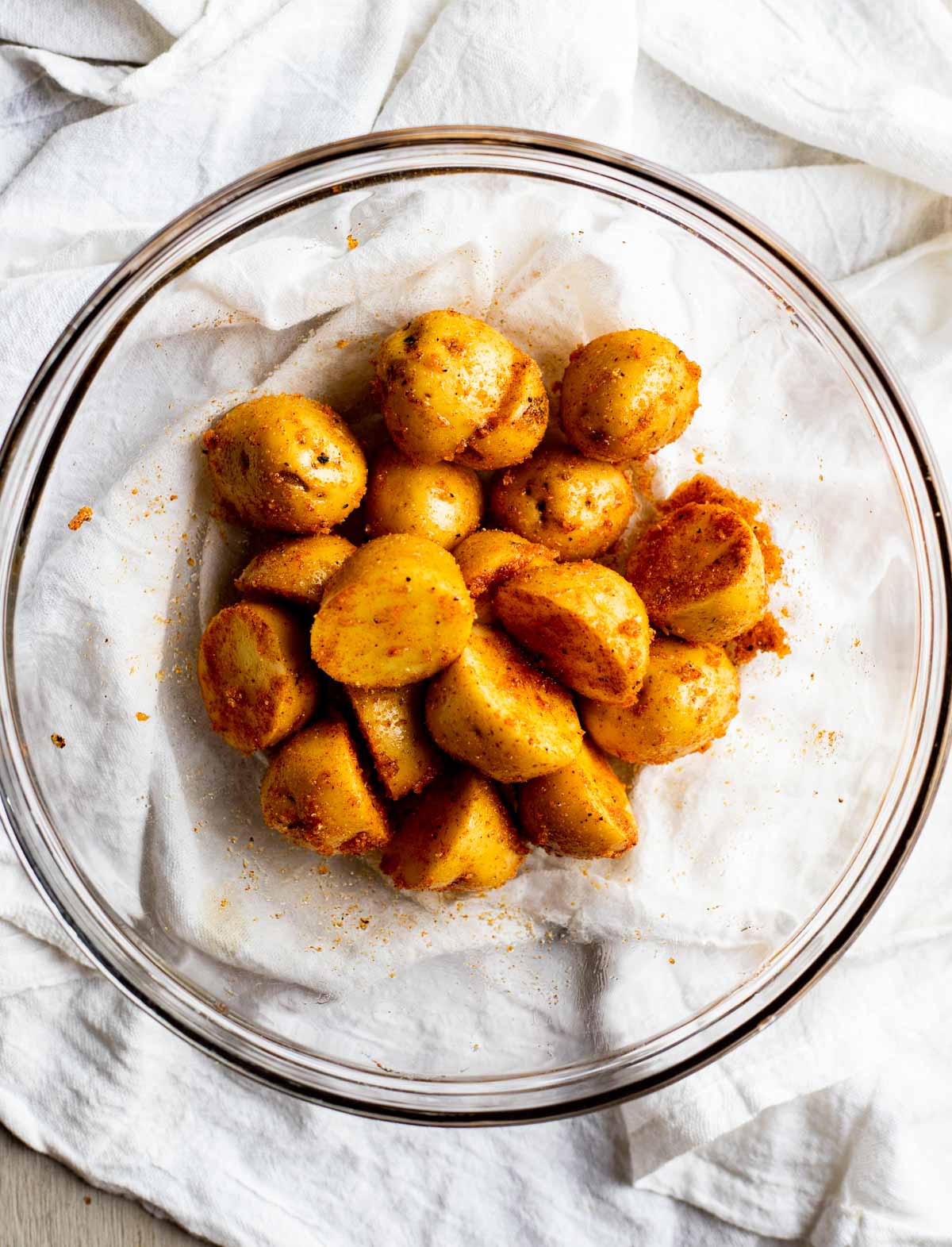 Mini potatoes cut in half and seasoned in a glass bowl on top of a white cloth.