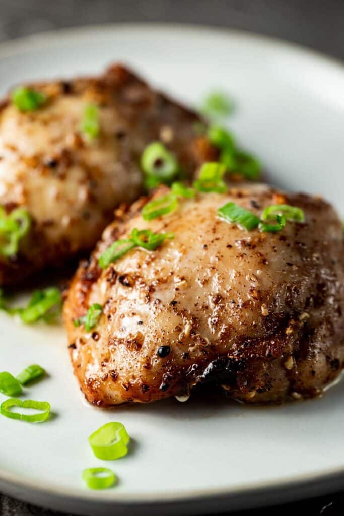 Side view of air fryer chicken thighs with chopped green onions on top.