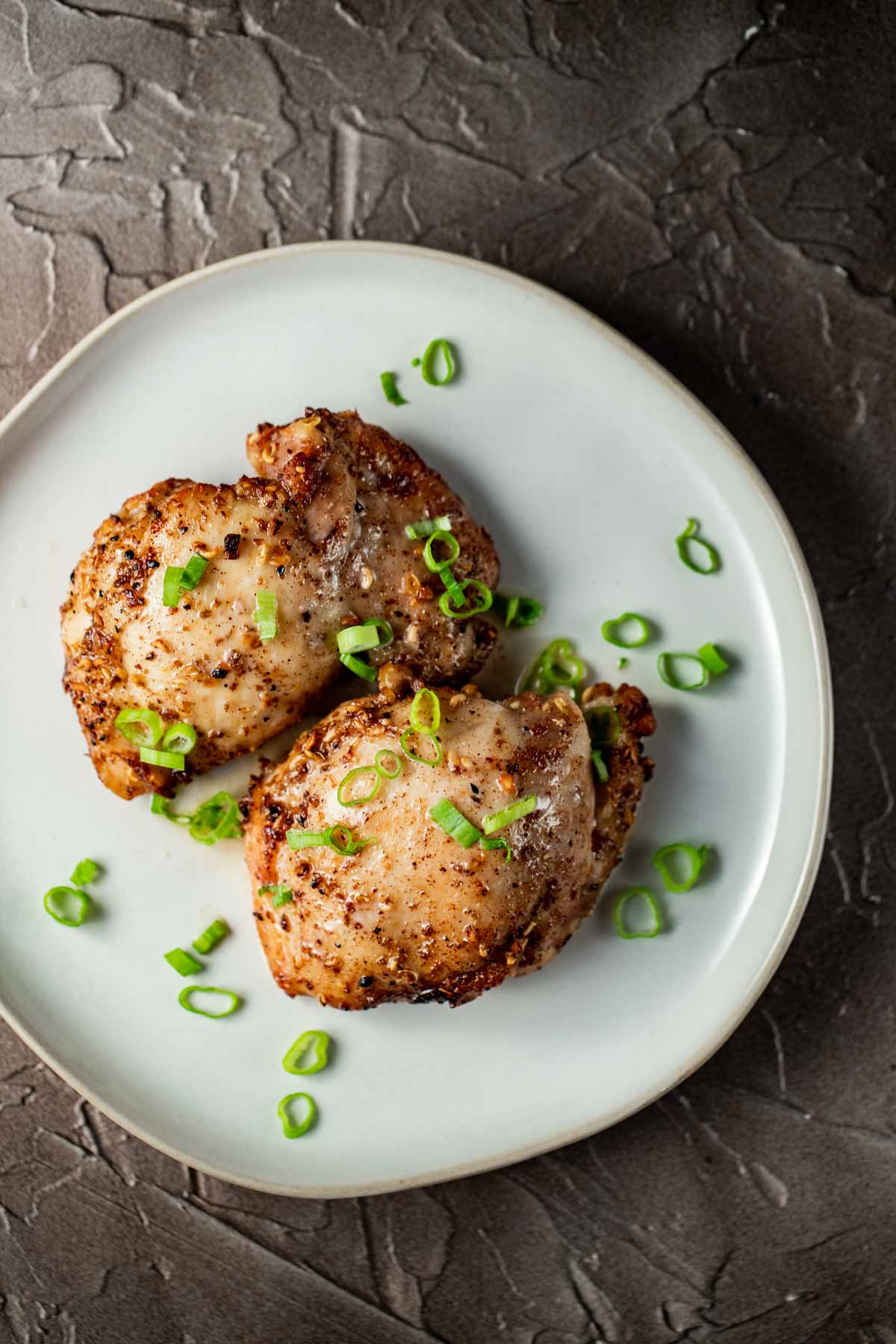 Air fryer boneless skinless chicken thighs on a white plate and topped with green onions.