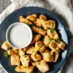 Overhead view of chicken bites on a blue plate with a bowl of dipping sauce on the side.