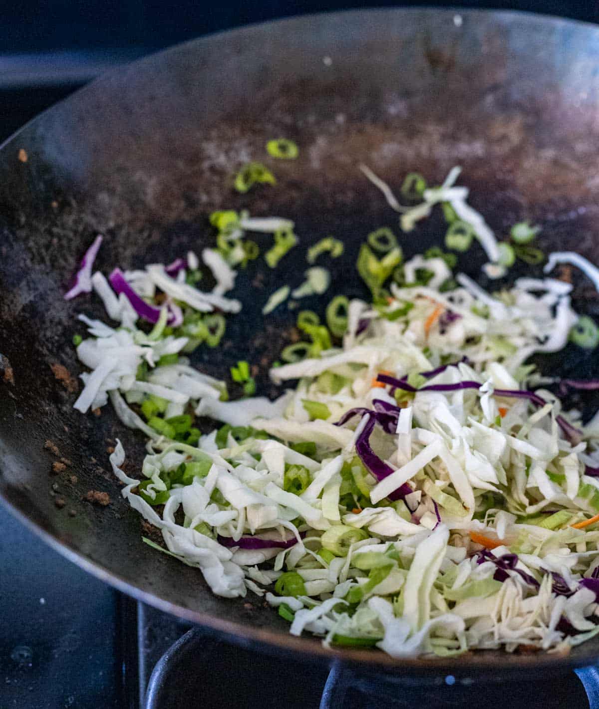 Shredded cabbage in a wok on the stovetop.
