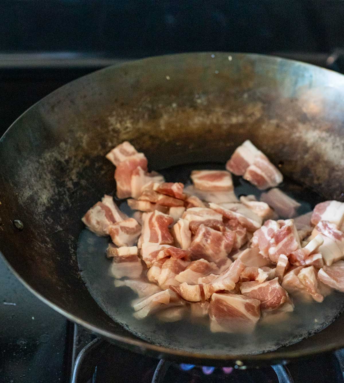 Pork belly pieces in liquid in a wok on the stovetop.