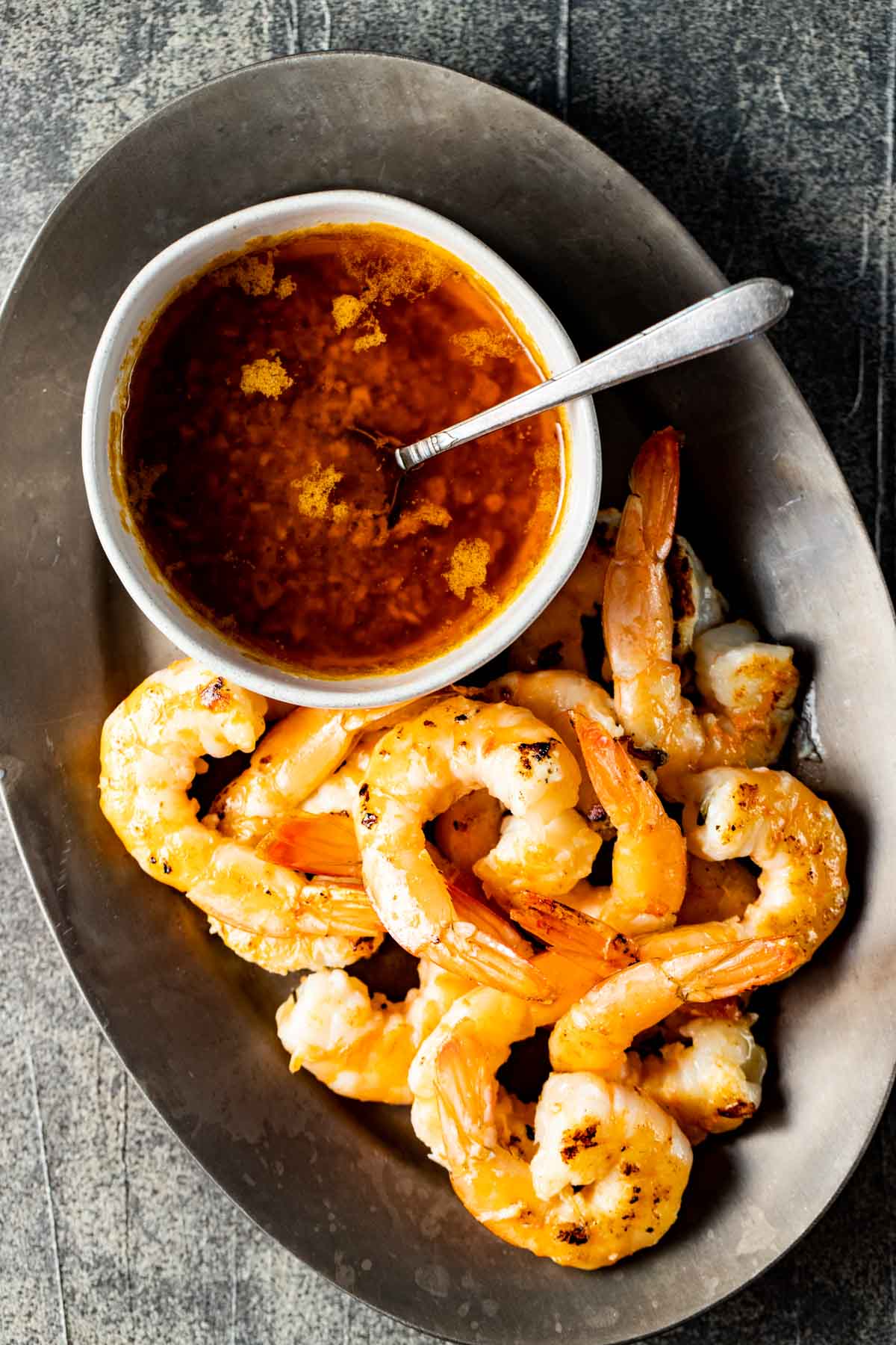 A bowl of seafood butter sauce on a platter with shrimp on the side.