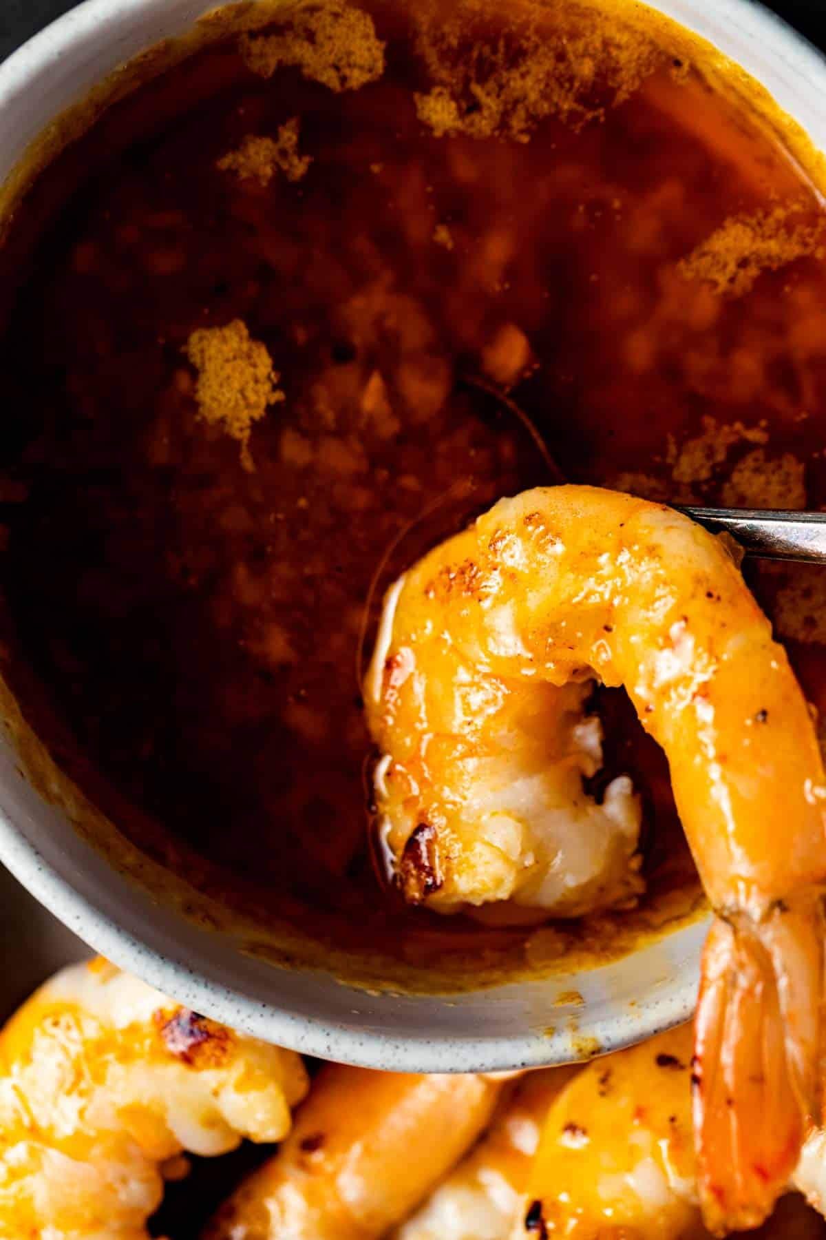 Close up view of shrimp dipped in the small bowl of seafood butter sauce.