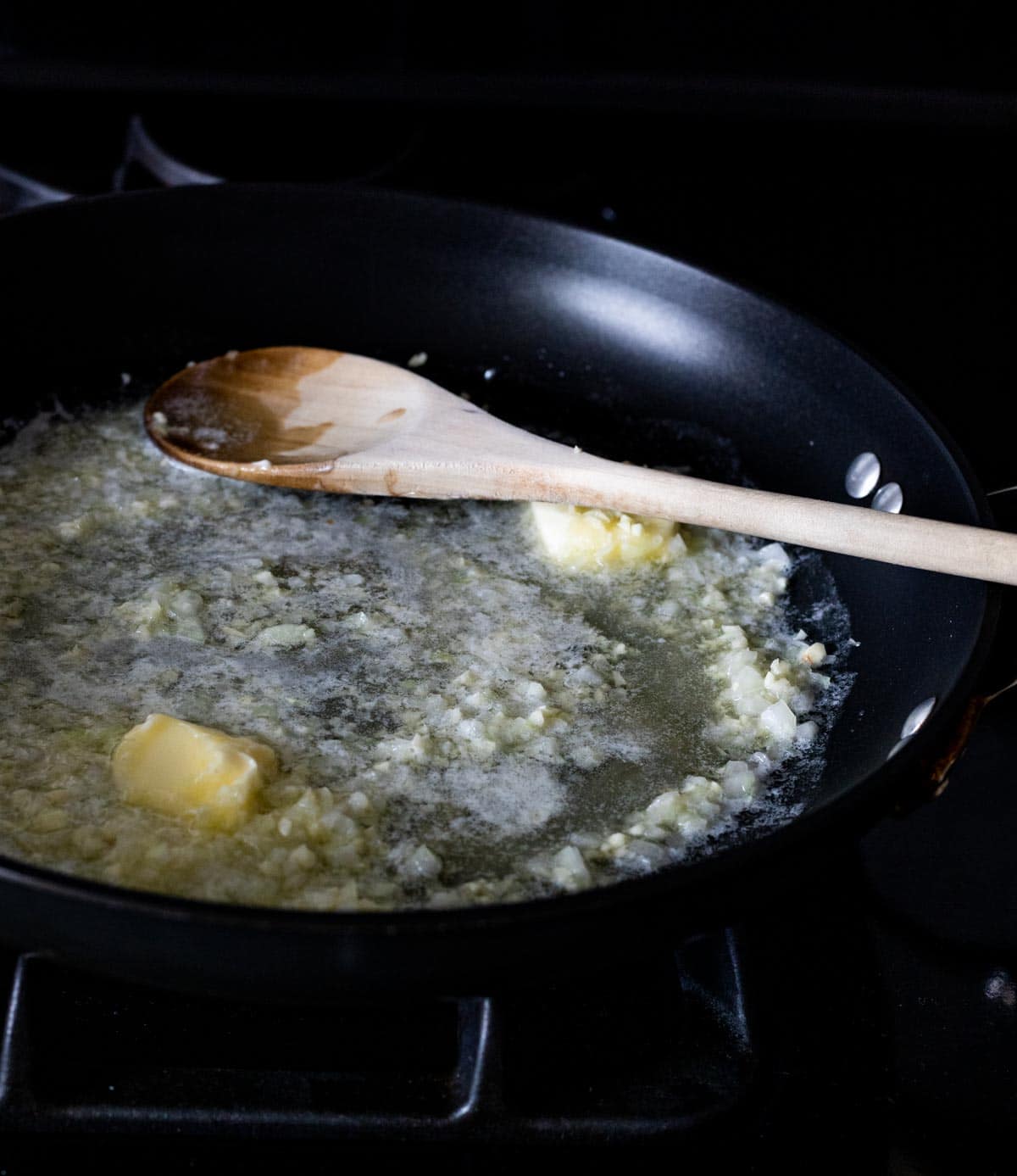 Butter, onion and garlic cooking in a skillet on the stovetop.