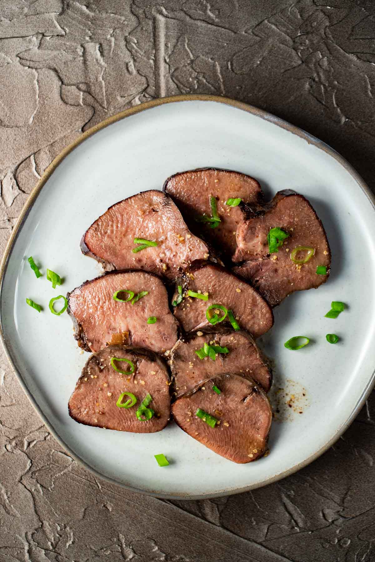 Slices of beef tongue arranged on a white plate.