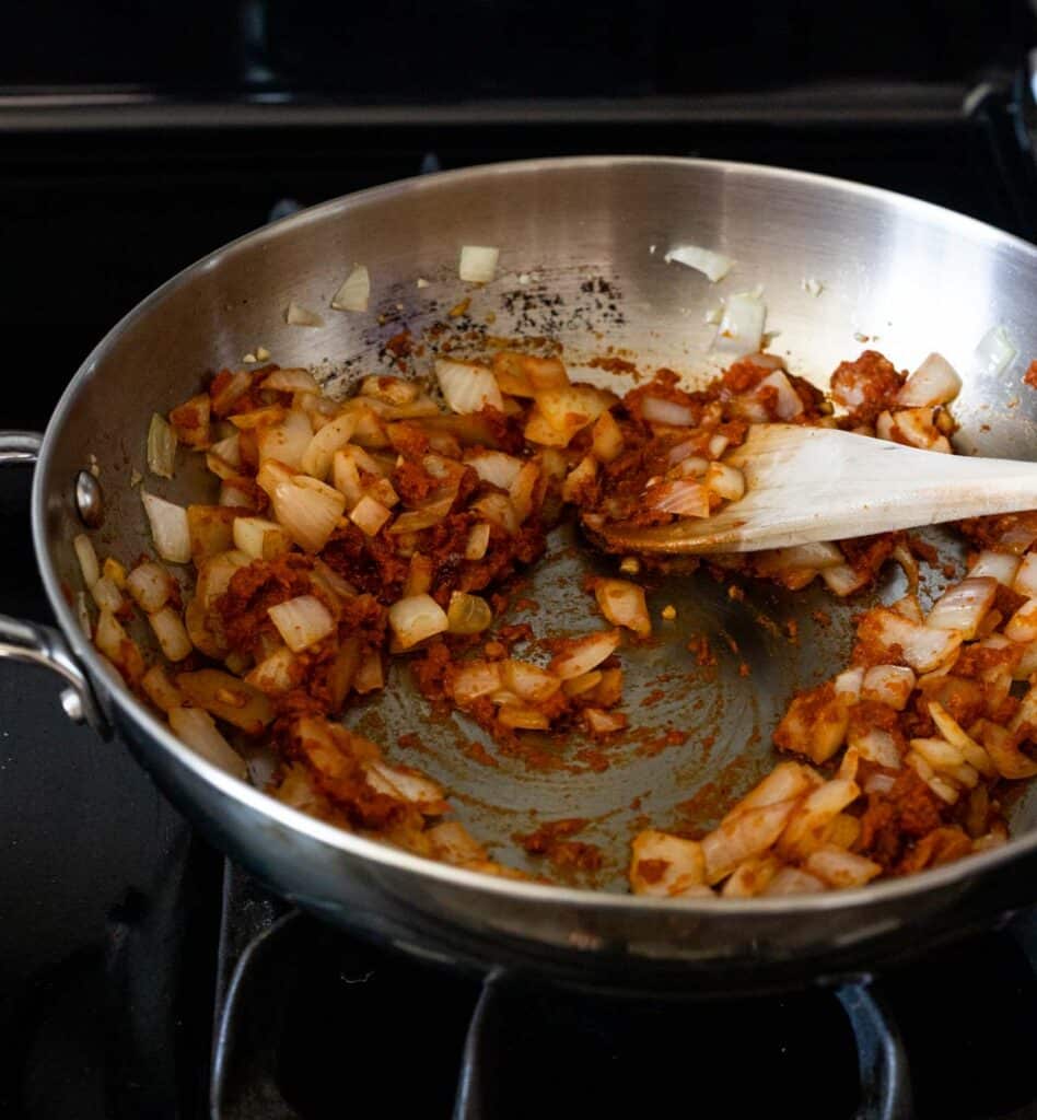 Onion, curry paste and other ingredients sautéing in a skillet on the stovetop.