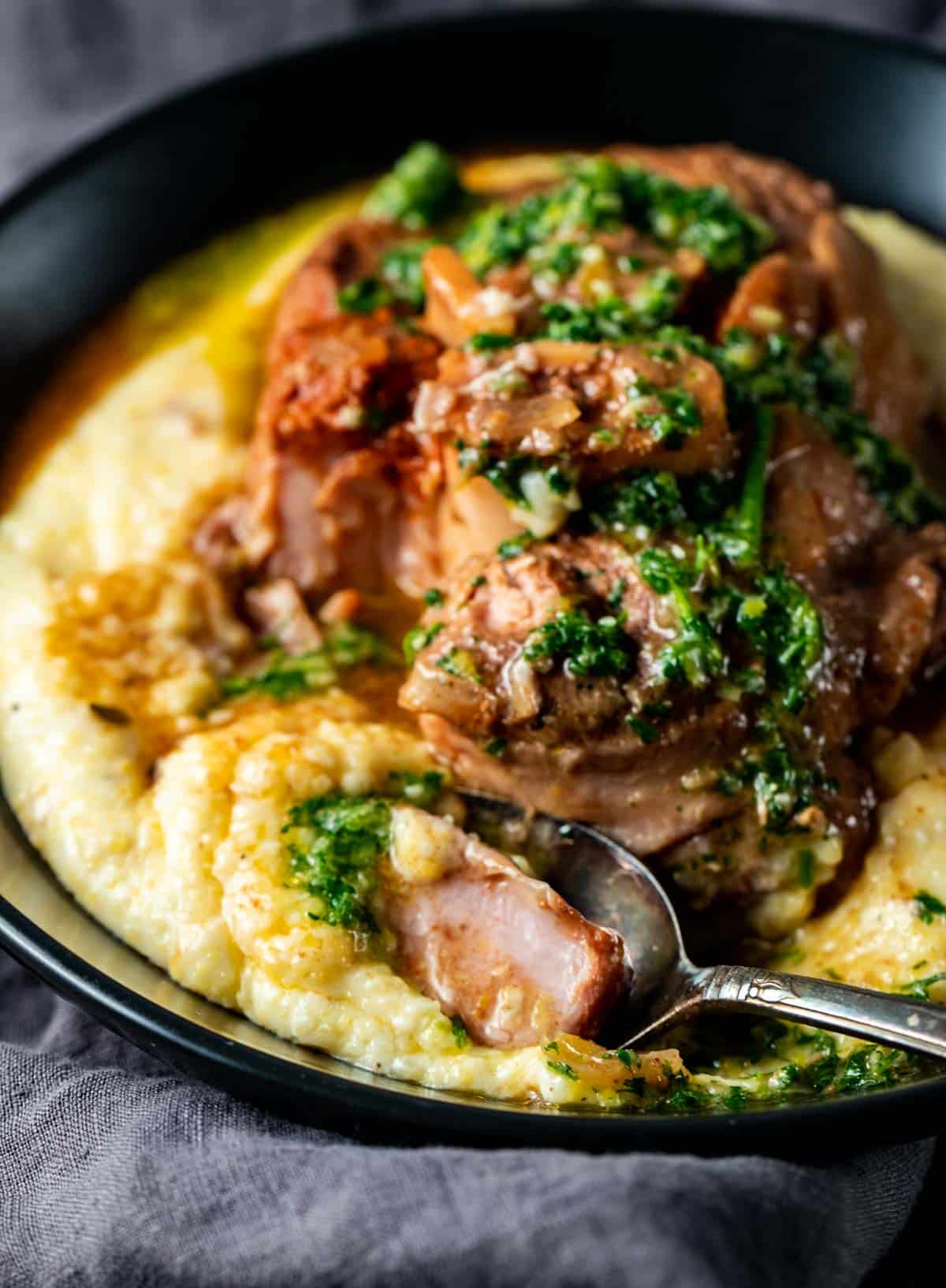 Side view of a spoonful of osso buco and polenta being taken from a bowl.