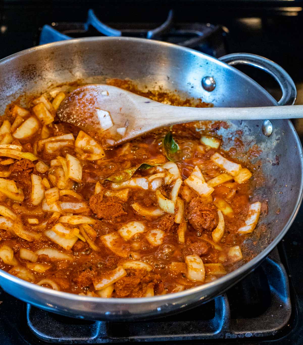 Onions and curry paste being stirred around in a skillet with a wooden spoon.