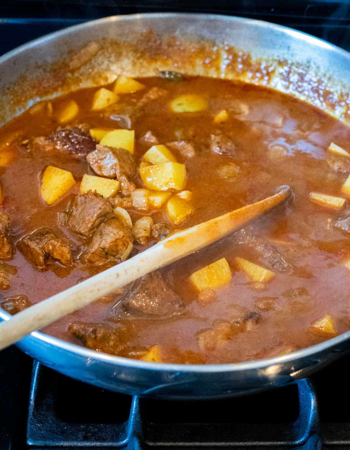Beef massaman curry simmering in a skillet on the stovetop.