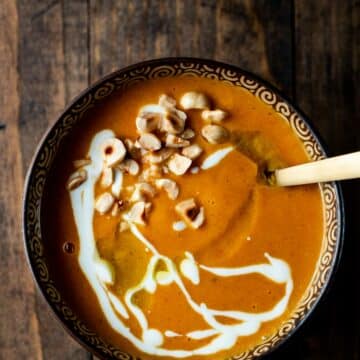 orange colored soup drizzled with white sauce and nuts