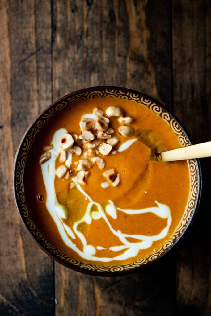 orange colored soup drizzled with white sauce and nuts