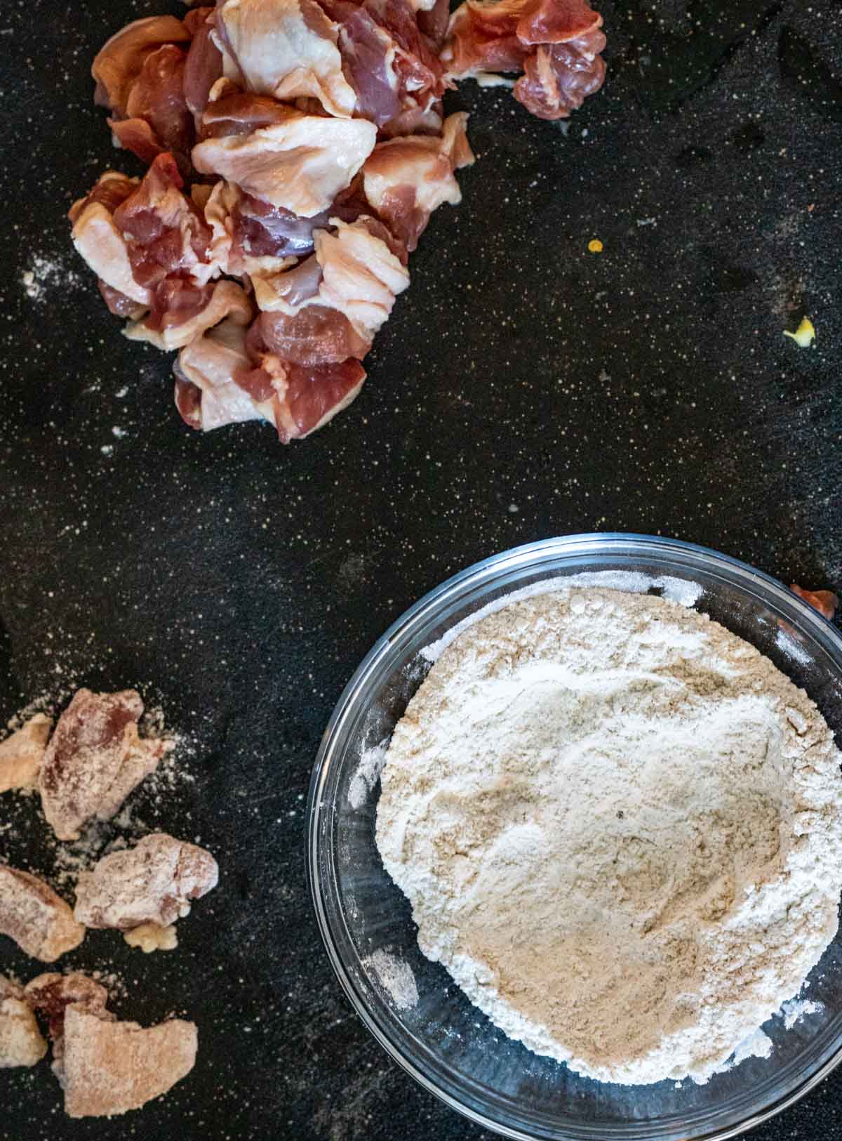 Duck pieces on a work surface with a bowl of the flour mixture and some floured duck bites on the side.