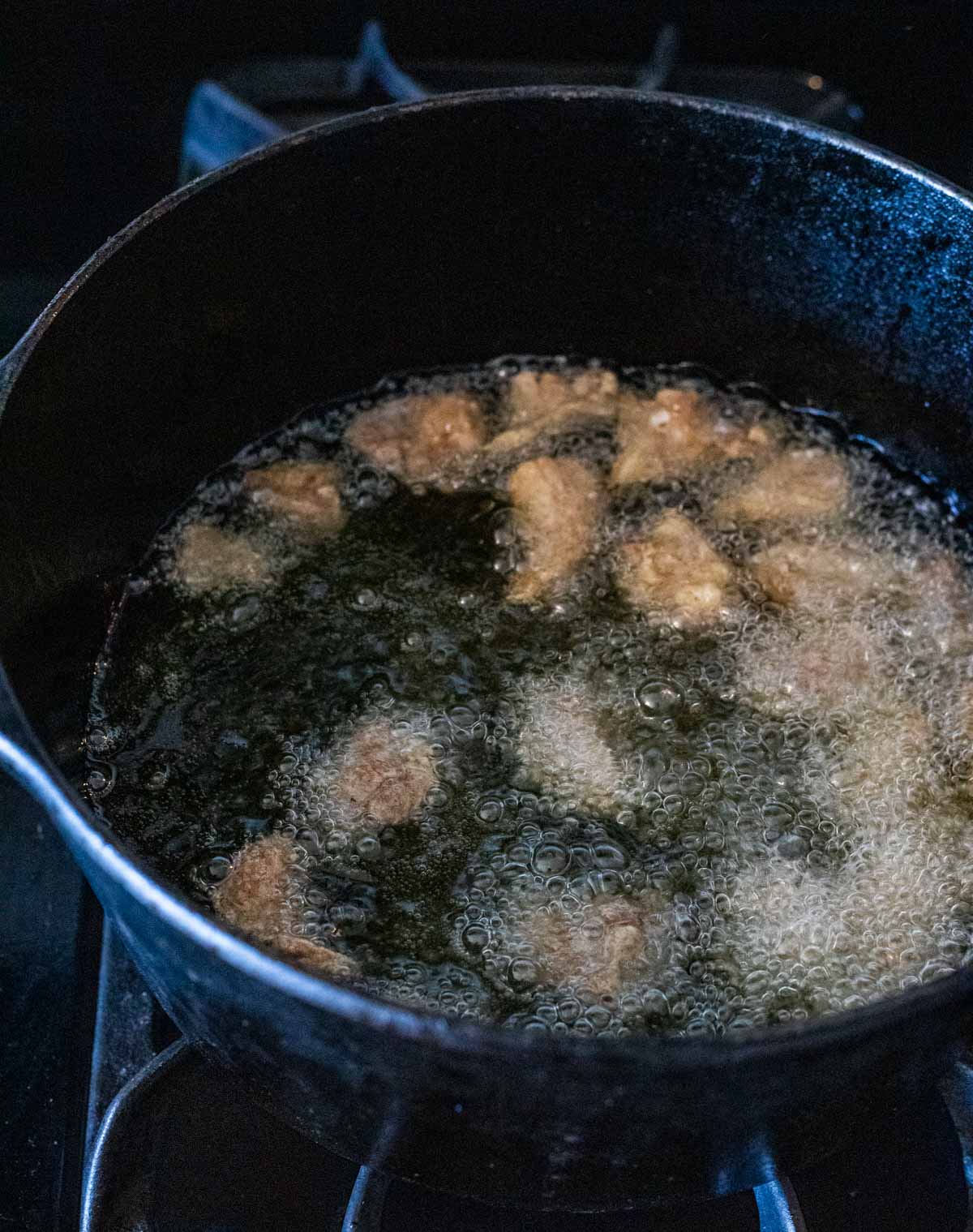 Duck bites frying in oil in a Dutch oven on the stovetop.