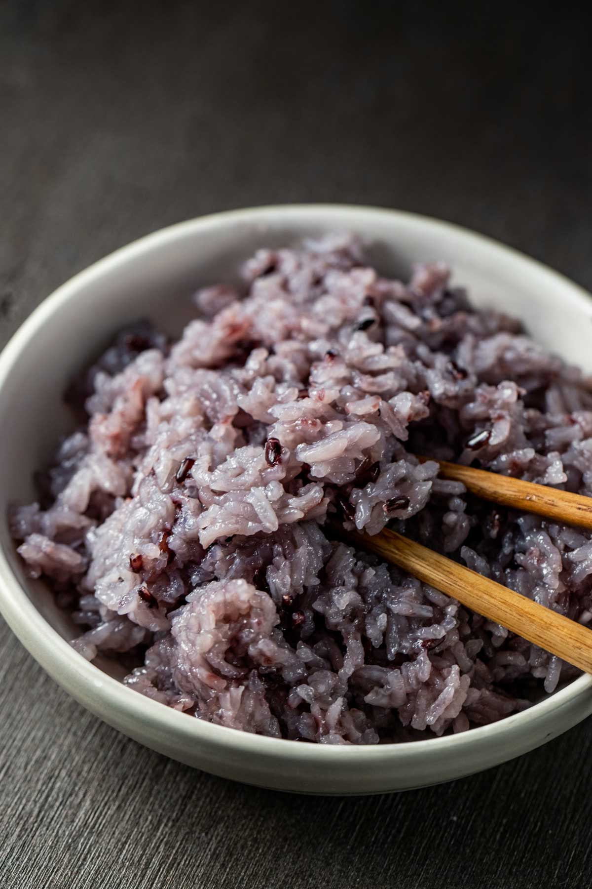 Side view of Korean purple rice served in a white bowl with chopsticks.