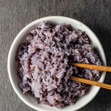 Overhead view of purple rice in a bowl with chopsticks inserted into it.