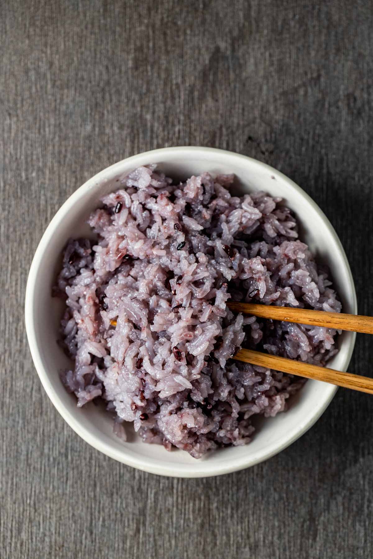 Overhead view of purple rice in a bowl with chopsticks inserted into it.