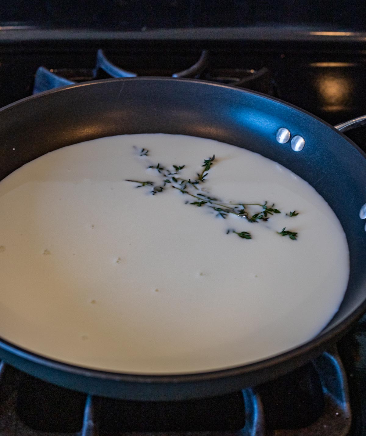Milk and thyme in a skillet on the stovetop.