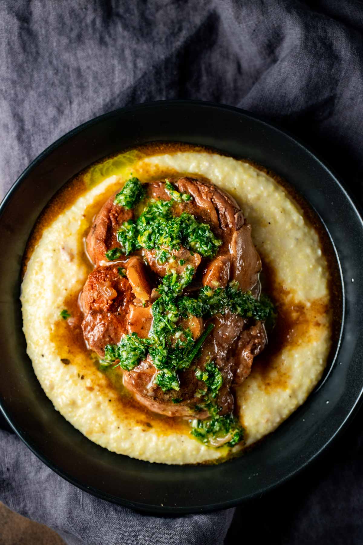 Overhead view of sous vide osso buco served on polenta with gremolata as garnish.