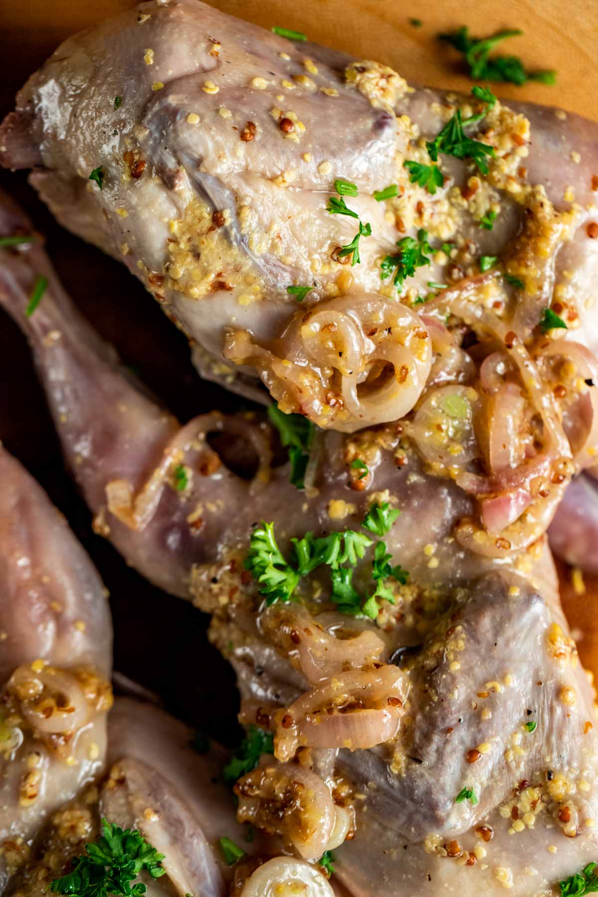 Close up view of cooked quail with shallots, herbs and other seasonings on top.