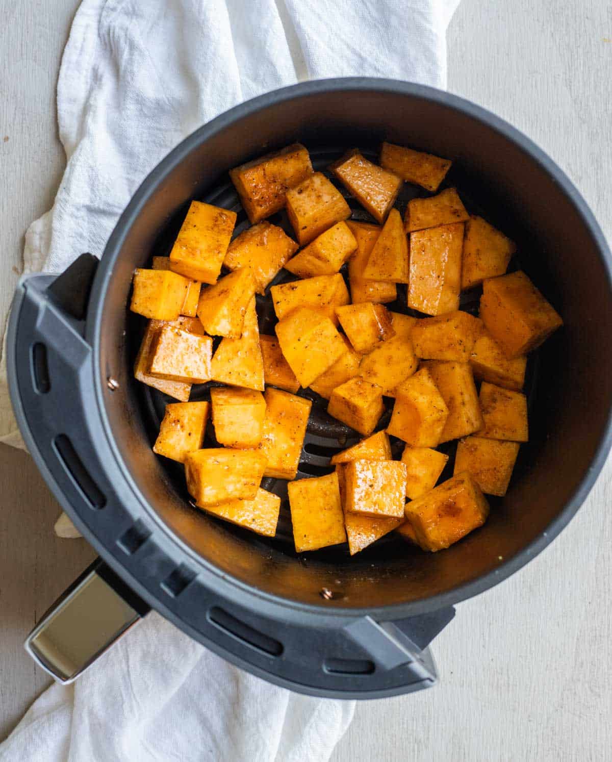 Seasoned pumpkin chunks in an air fryer basket.