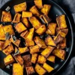 Overhead view of air fried pumpkin cubes on a black plate.