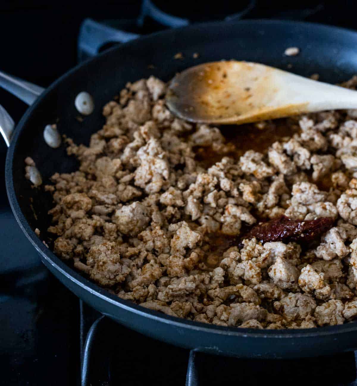 ground pork in a pan with a wooden spoon