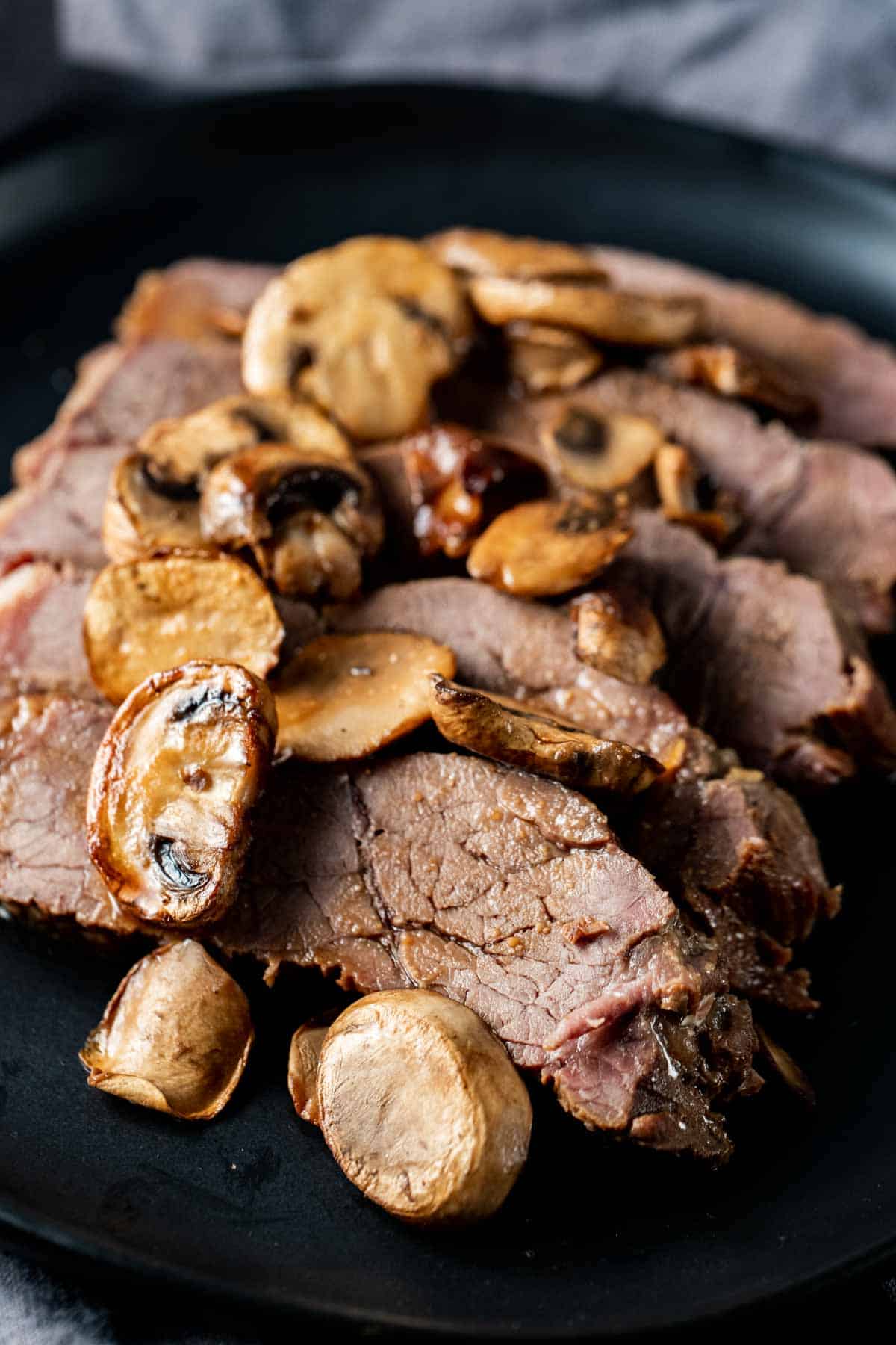 Close up view of sliced London broil topped with mushrooms.