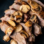 London broil topped with mushrooms and served on a black plate.