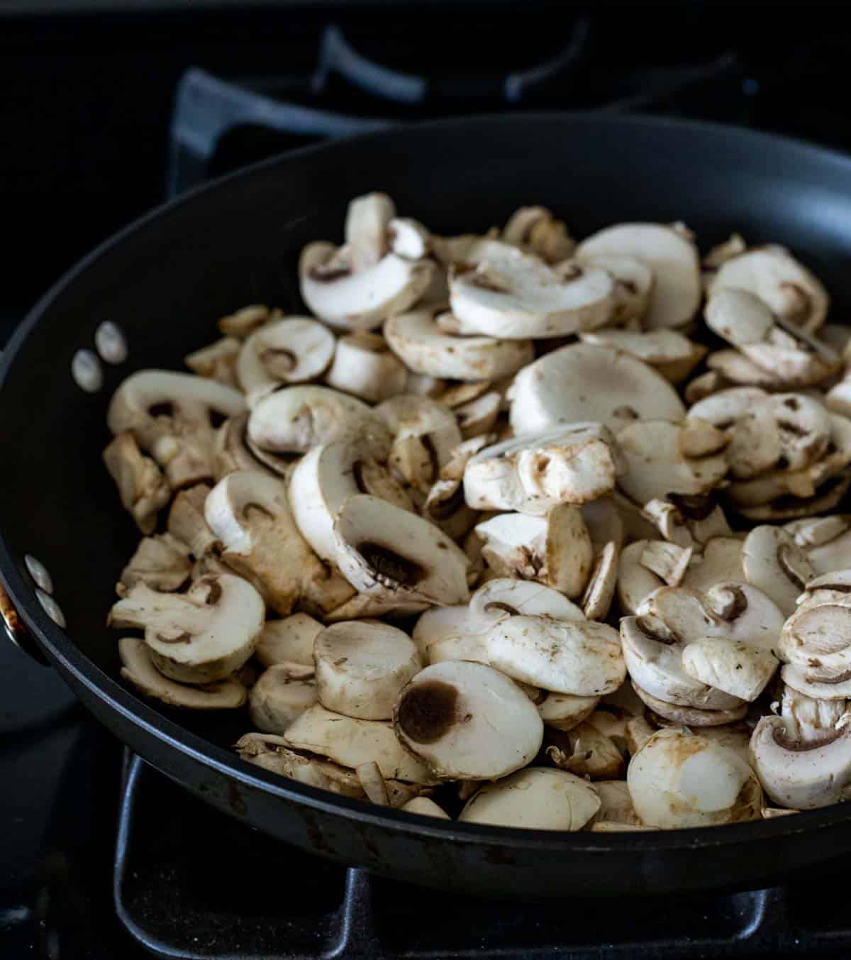 Sliced fresh mushrooms in a skillet on the stovetop.