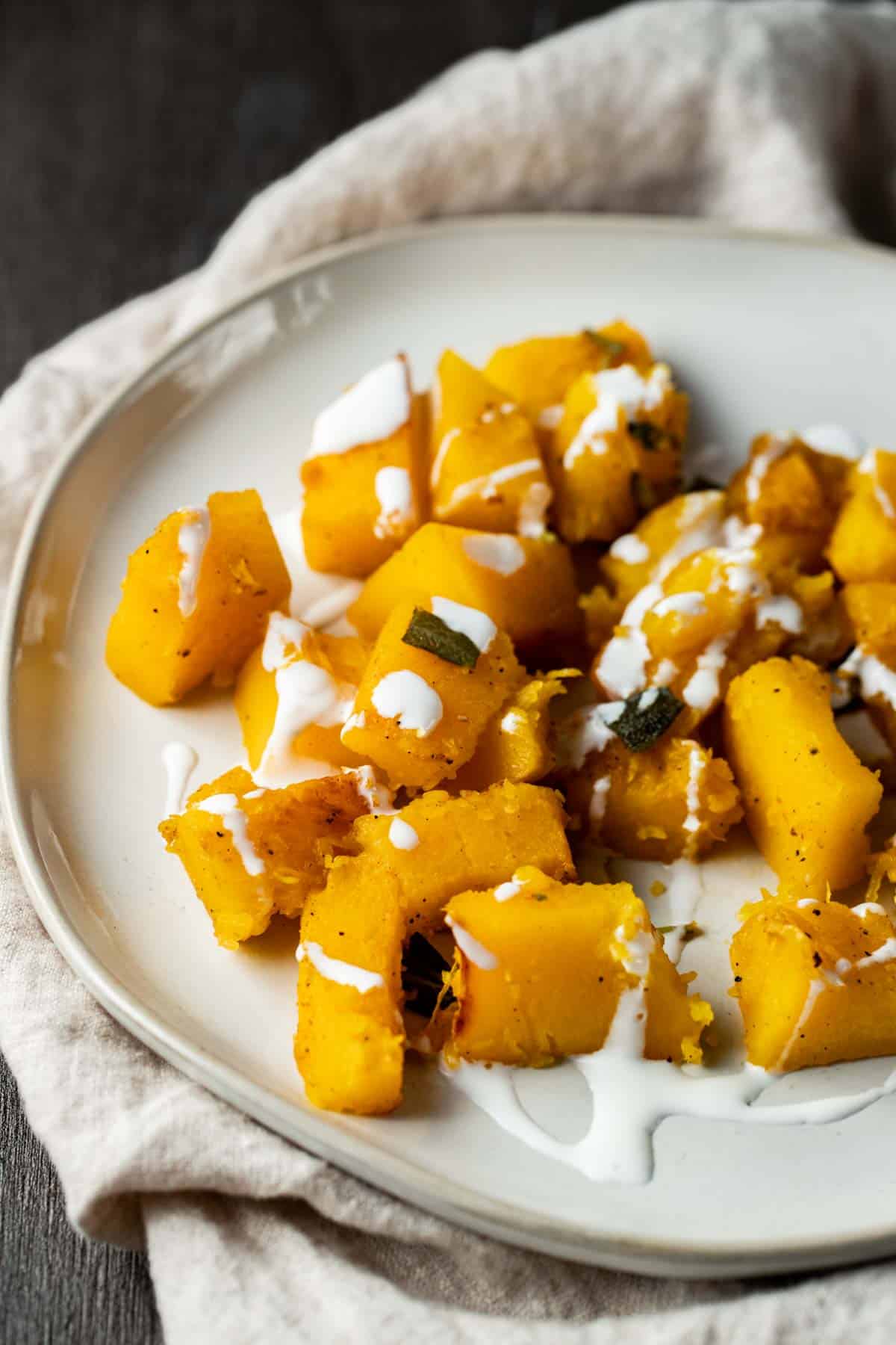Cooked pumpkin cubes on a plate, drizzled with crème fraiche.