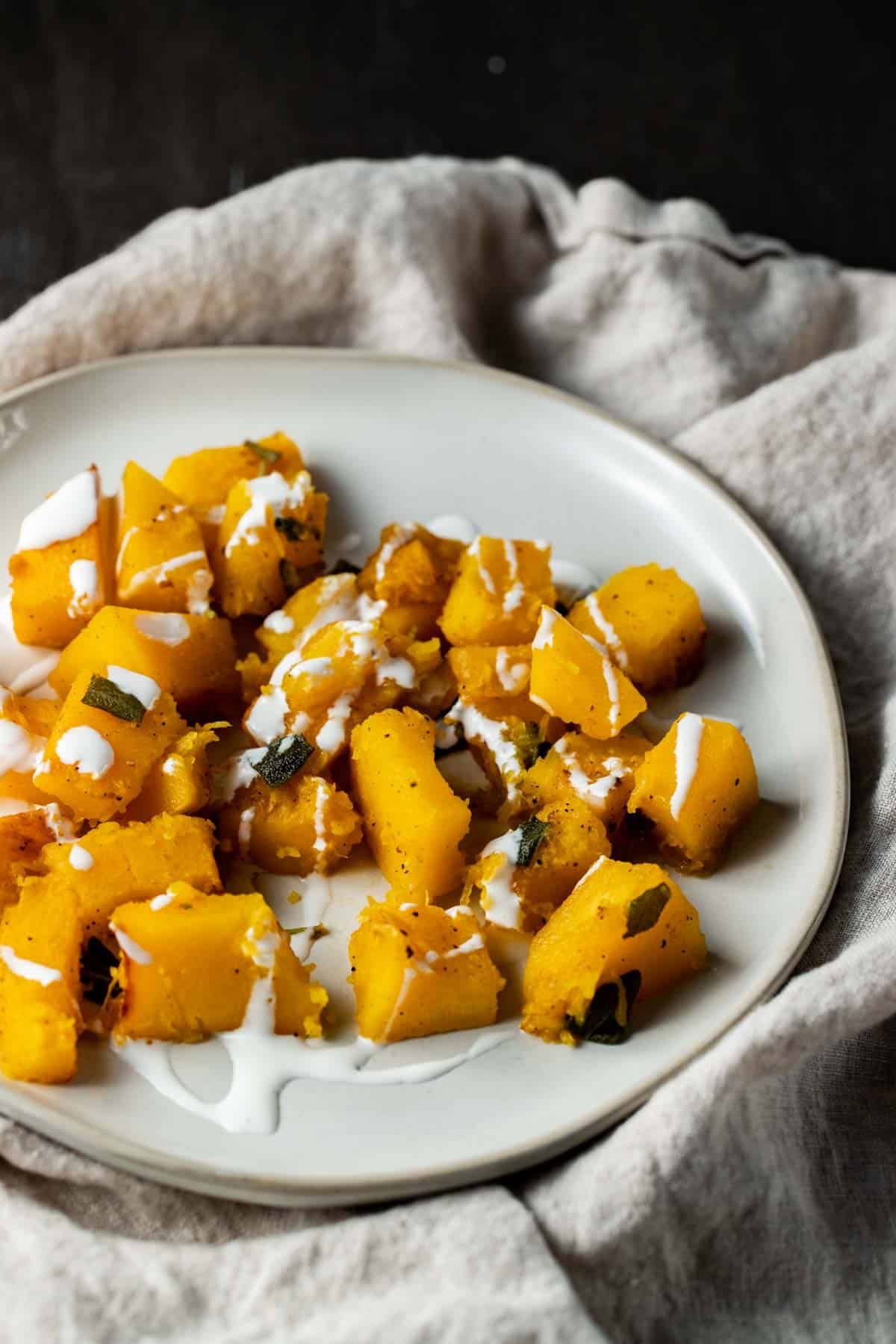 Cooked pumpkin cubes on a white plate on top of a grey cloth.