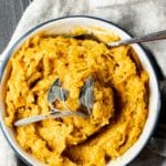 Overhead view of mashed pumpkin in a bowl with a spoon inserted into it.