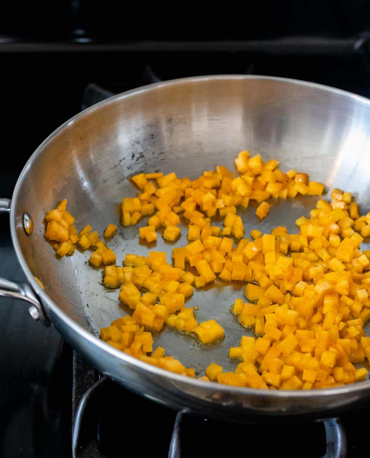 Diced pumpkin browning in a high sided skillet on the stovetop.