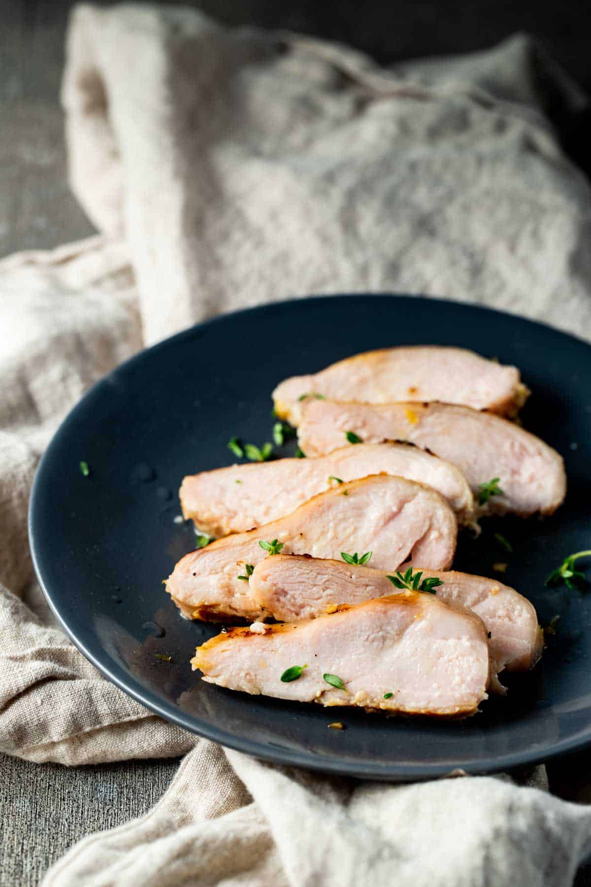 Sliced chicken breast on a dark blue plate and topped with chopped herbs.