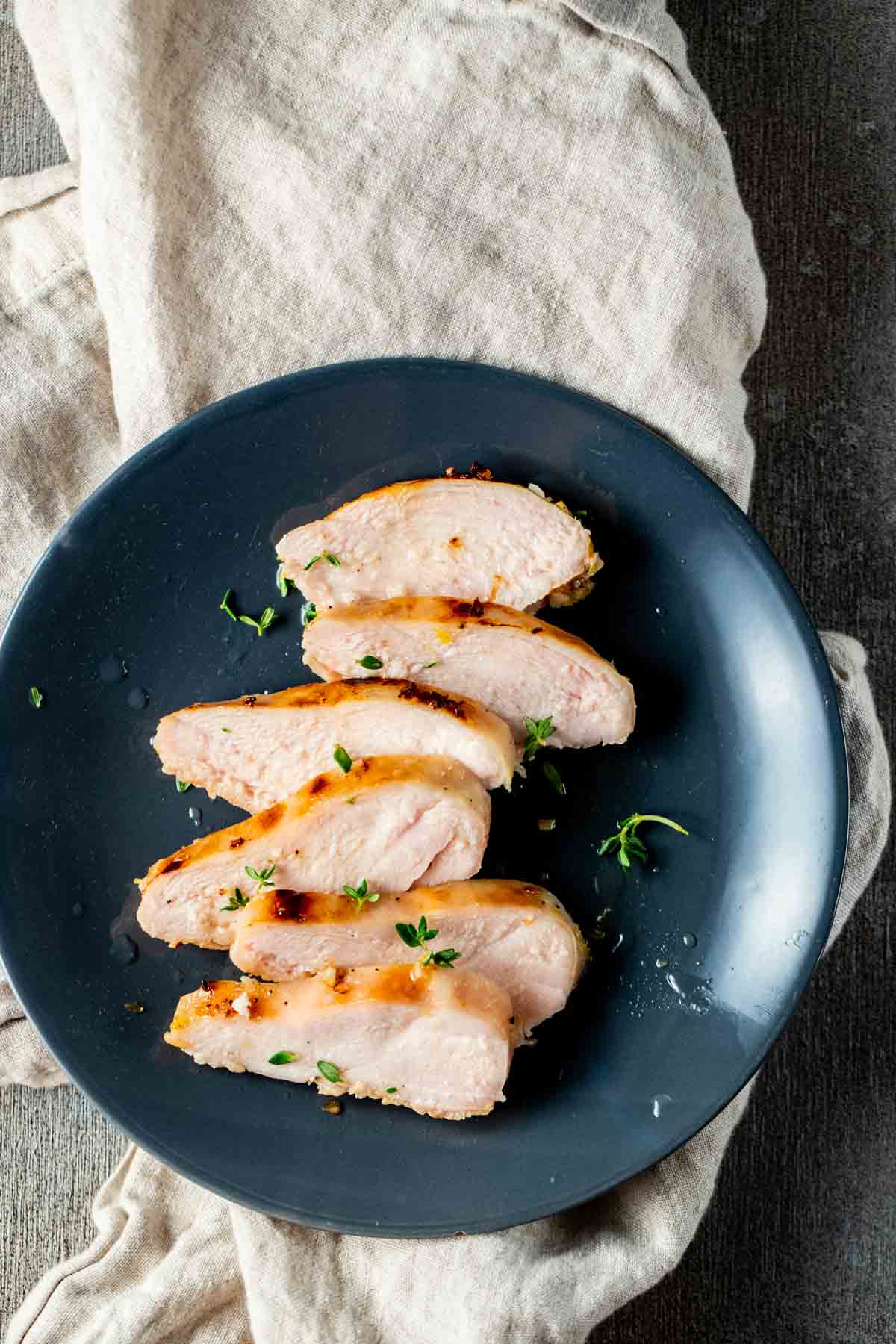 Overhead view of sliced chicken breast on a blue plate on top of a beige napkin.