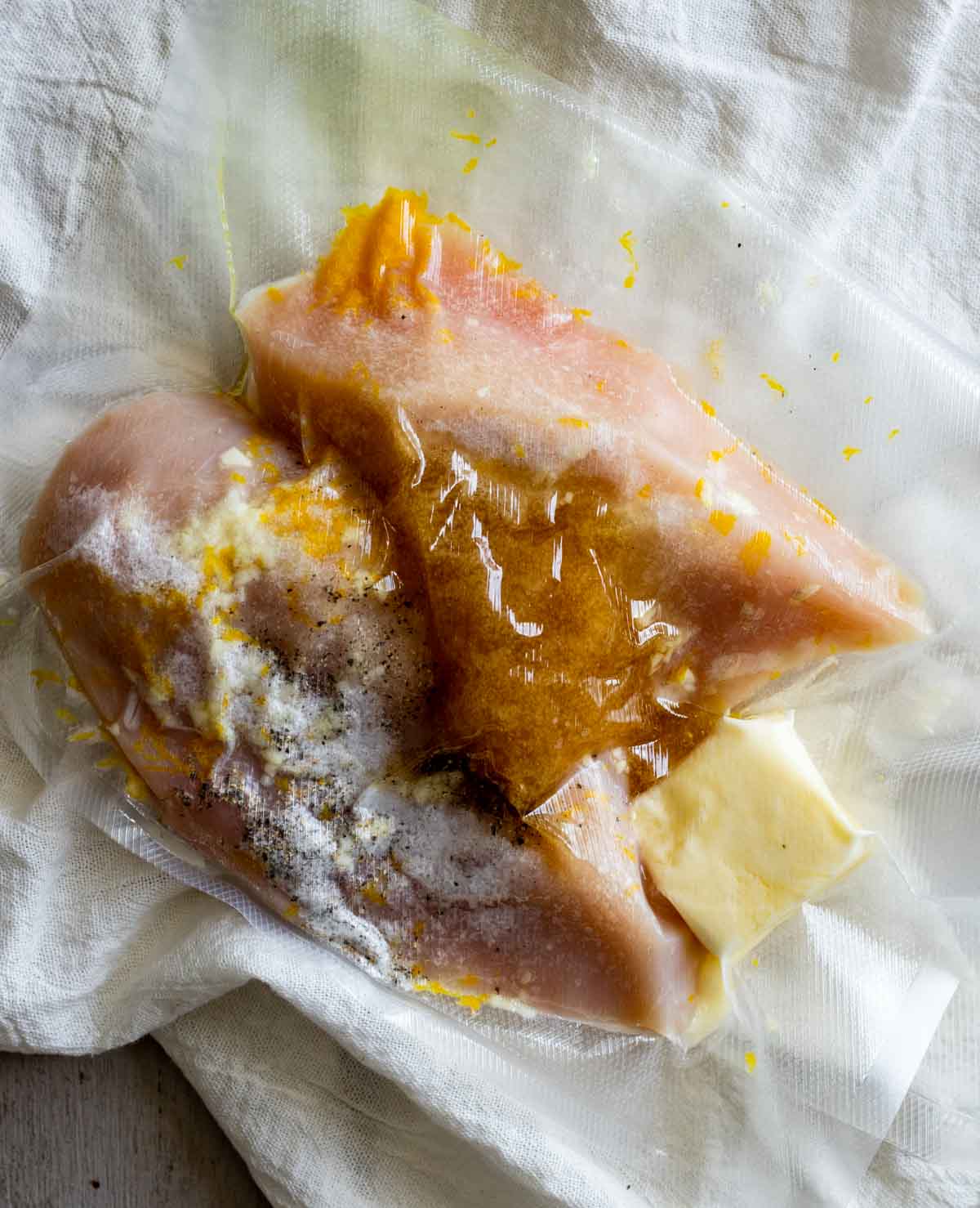 Two boneless, skinless chicken breasts in a vacuum sealed bag with butter and other ingredients.