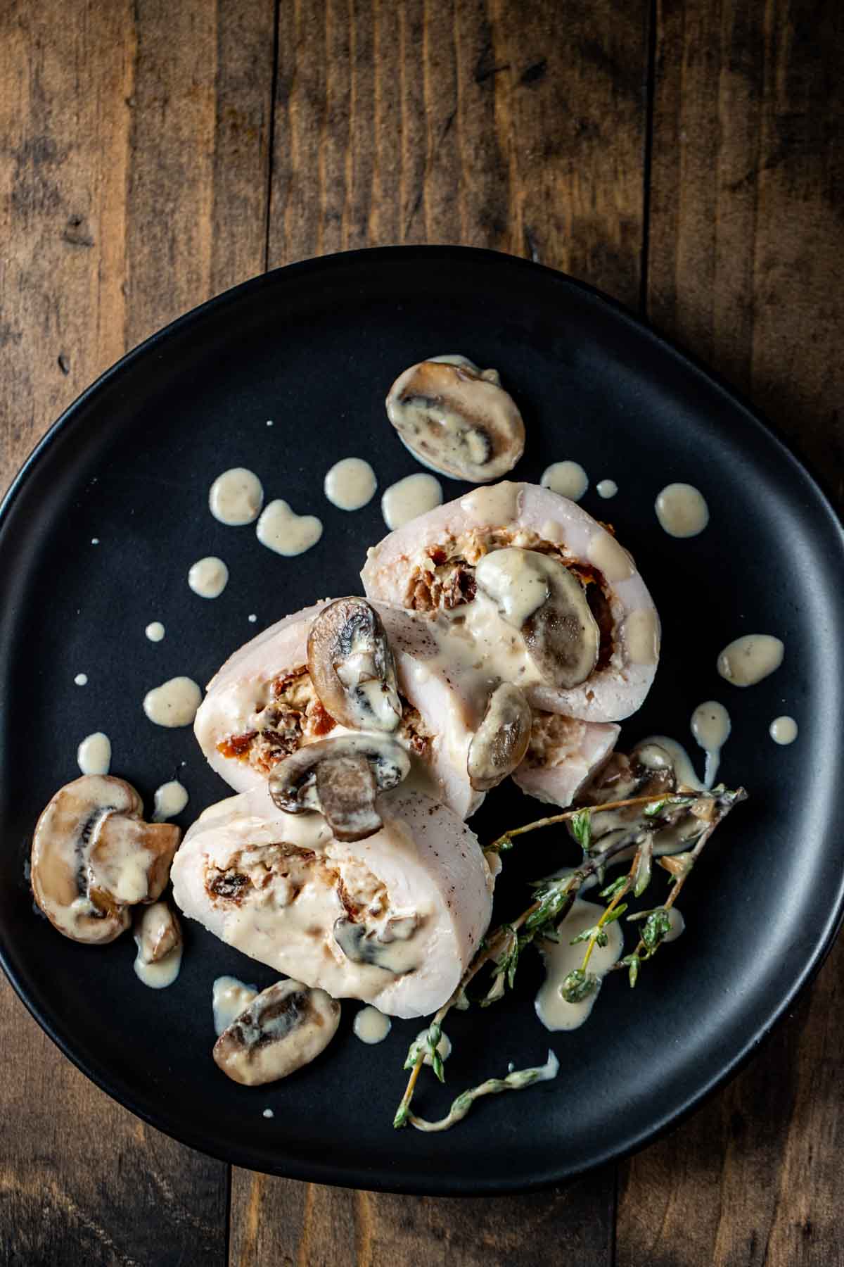 a plated stuffed chicken breast on a table with fresh thyme and a creamy mushroom sauce