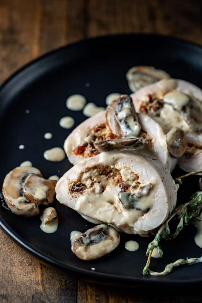 stuffed chicken breast with a creamy mushroom sauce on a black plate up close